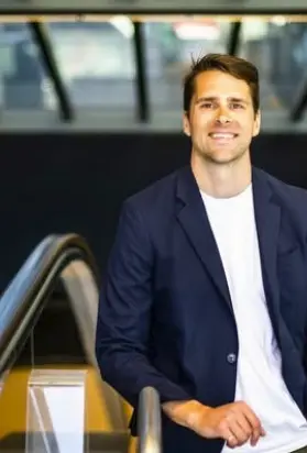 Nick Caros, MIT-trained transit researcher and city planner, smiling beside an escalator